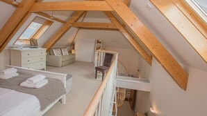 Een slaapkamer met een schuine kap, een bed met handdoeken, een dressoir, een stoel en een klein tafeltje met een plantje.