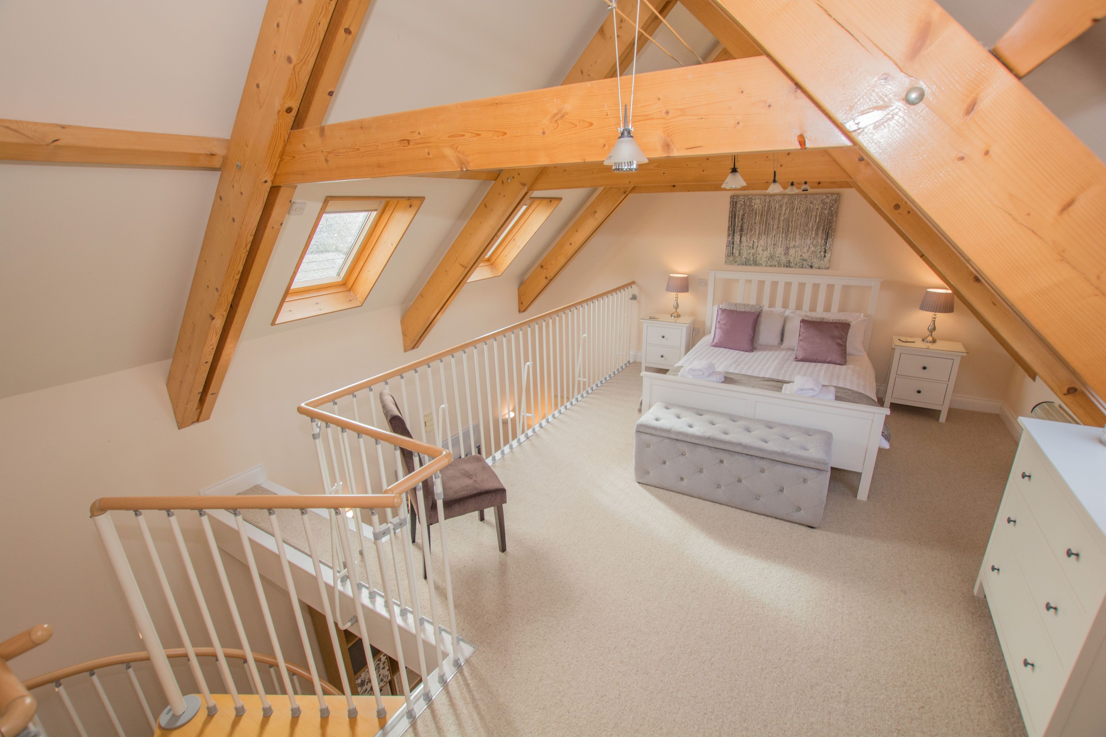 Ein Schlafzimmer mit Schrägdecke, einem Bett, einem Nachttisch, einer Kommode und einer Treppe mit Geländer.