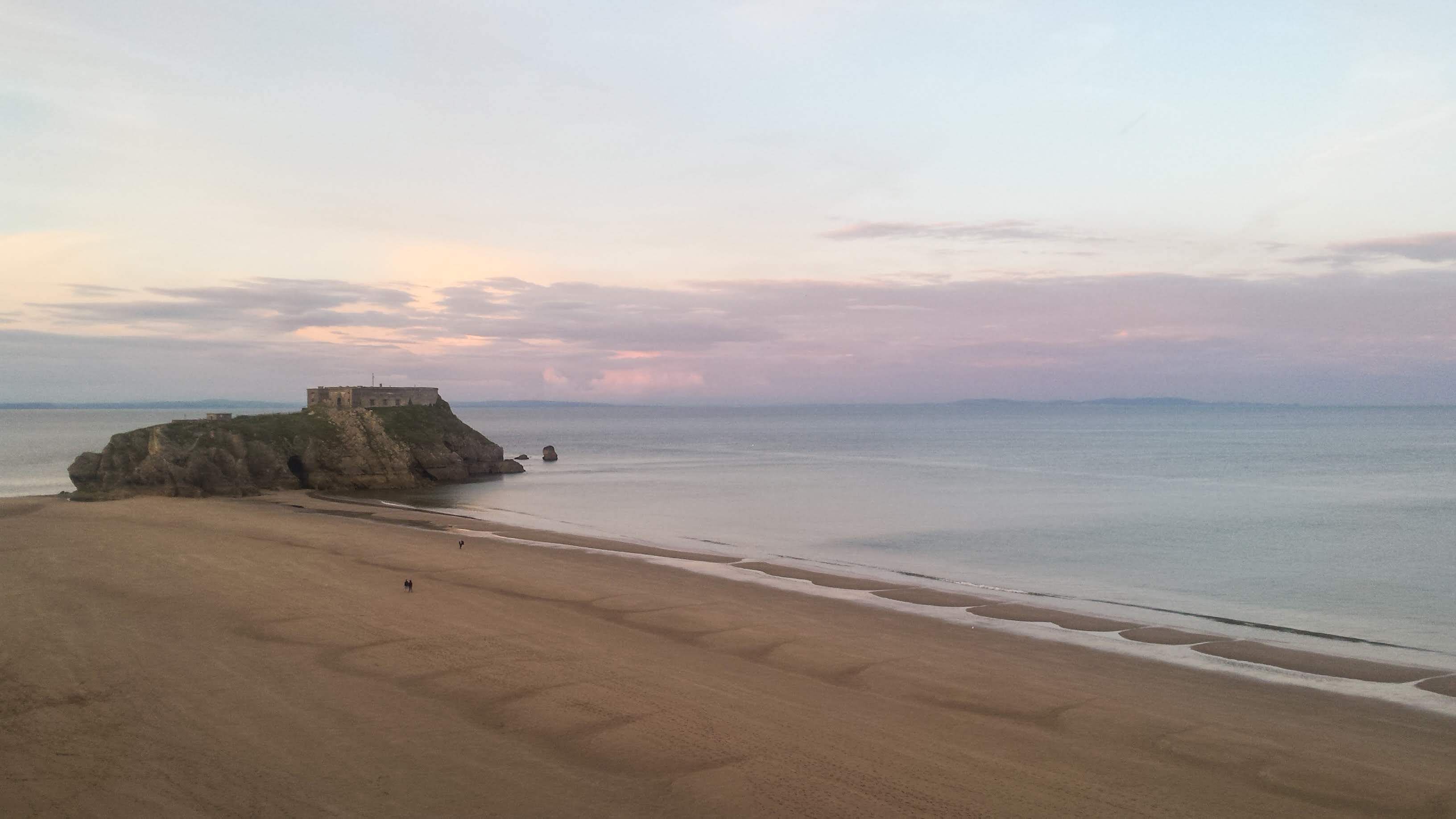 A beach with a rocky outcrop and a building on top.