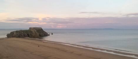 A beach with a rocky outcrop and a building on top.