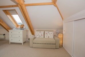 A bedroom with a sloped ceiling, a bed with floral pillows, a bedside table, and a floor lamp.