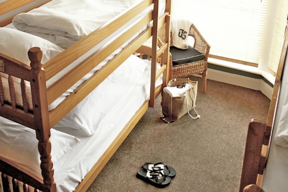 A bunk bed with a headboard, a wicker chair, a small table, and a hanging light fixture.
