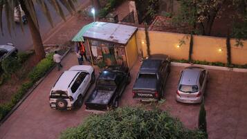 A parking area with several cars, including a Toyota pickup truck, and a small shop with a green awning.
