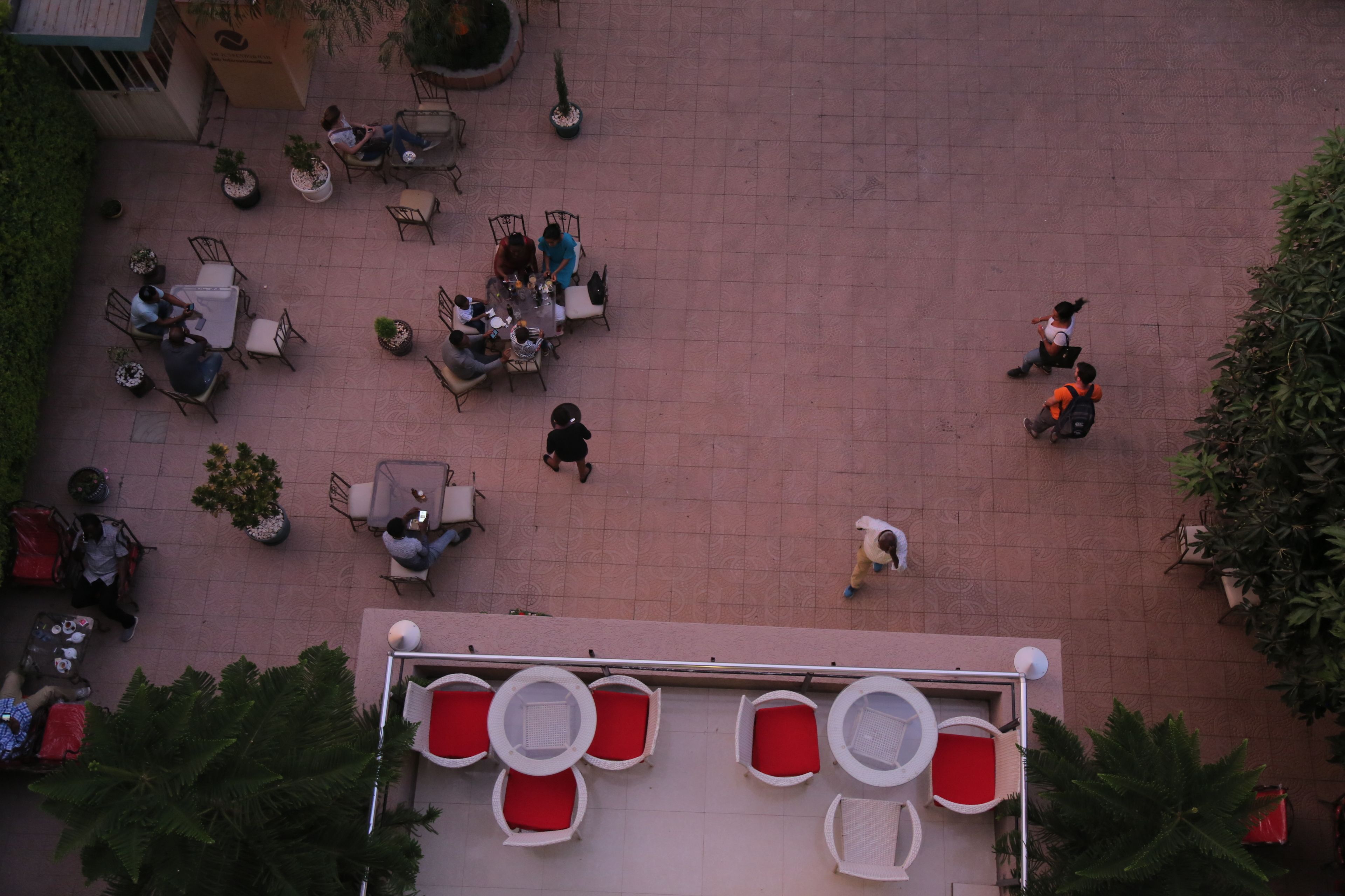 An aerial view of a courtyard with outdoor seating, potted plants, and a building with a distinctive red and white facade.