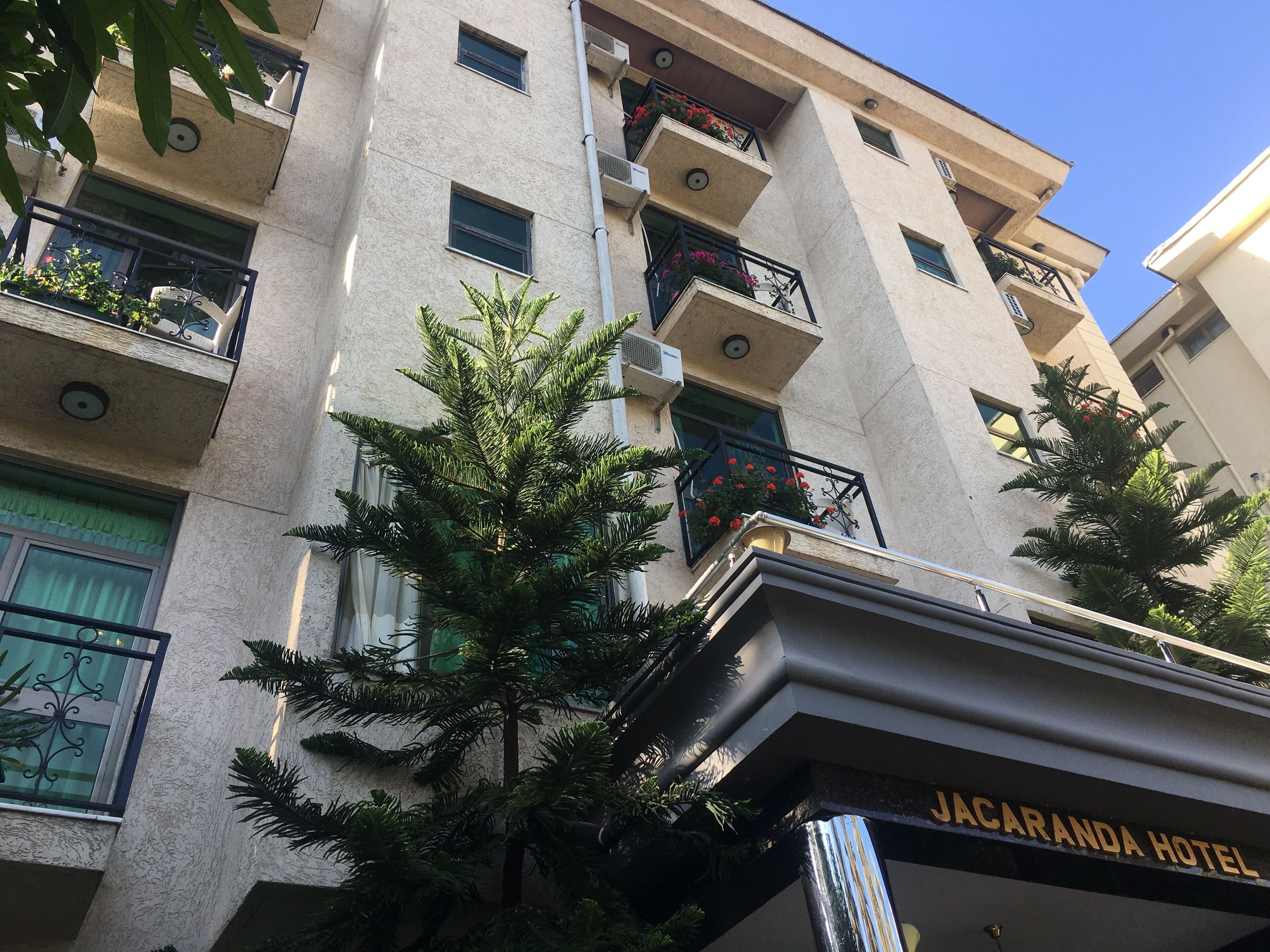 A building with multiple balconies, some with plants and flowers. The building has a sign that reads "JACARANDA HOTEL".
