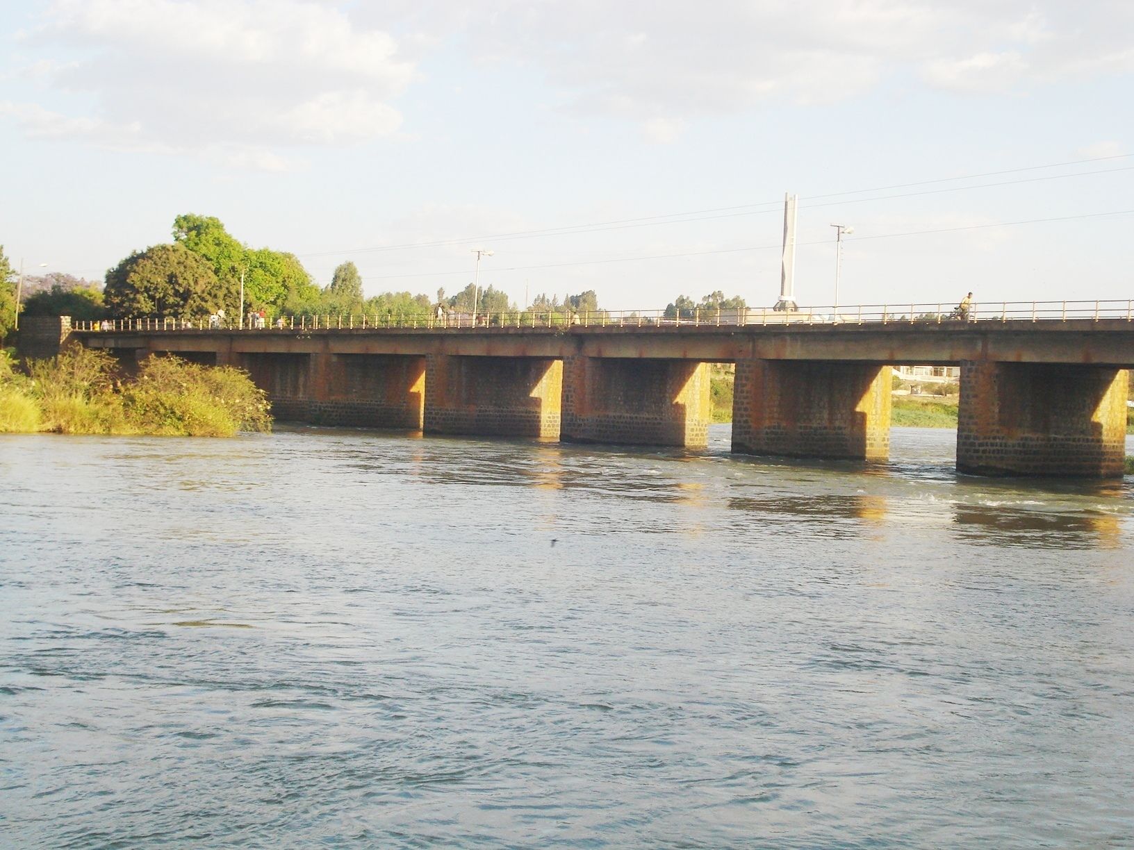 A bridge over a river with a pedestrian walkway and a white monument in the background.