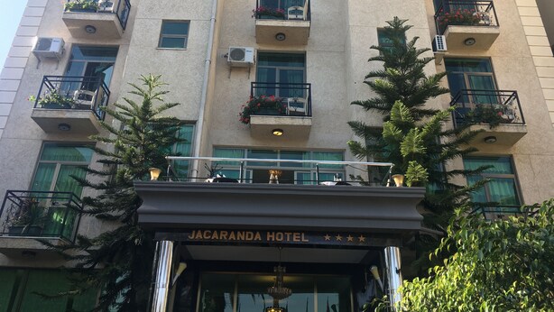 Un hôtel à plusieurs étages doté de balcons, de climatiseurs et d’une enseigne indiquant « HÔTEL JACARANDA ».
