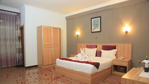Une chambre d’hôtel avec un lit en bois, une table de chevet avec un téléphone et une bouteille, une armoire et un luminaire fixé au mur.