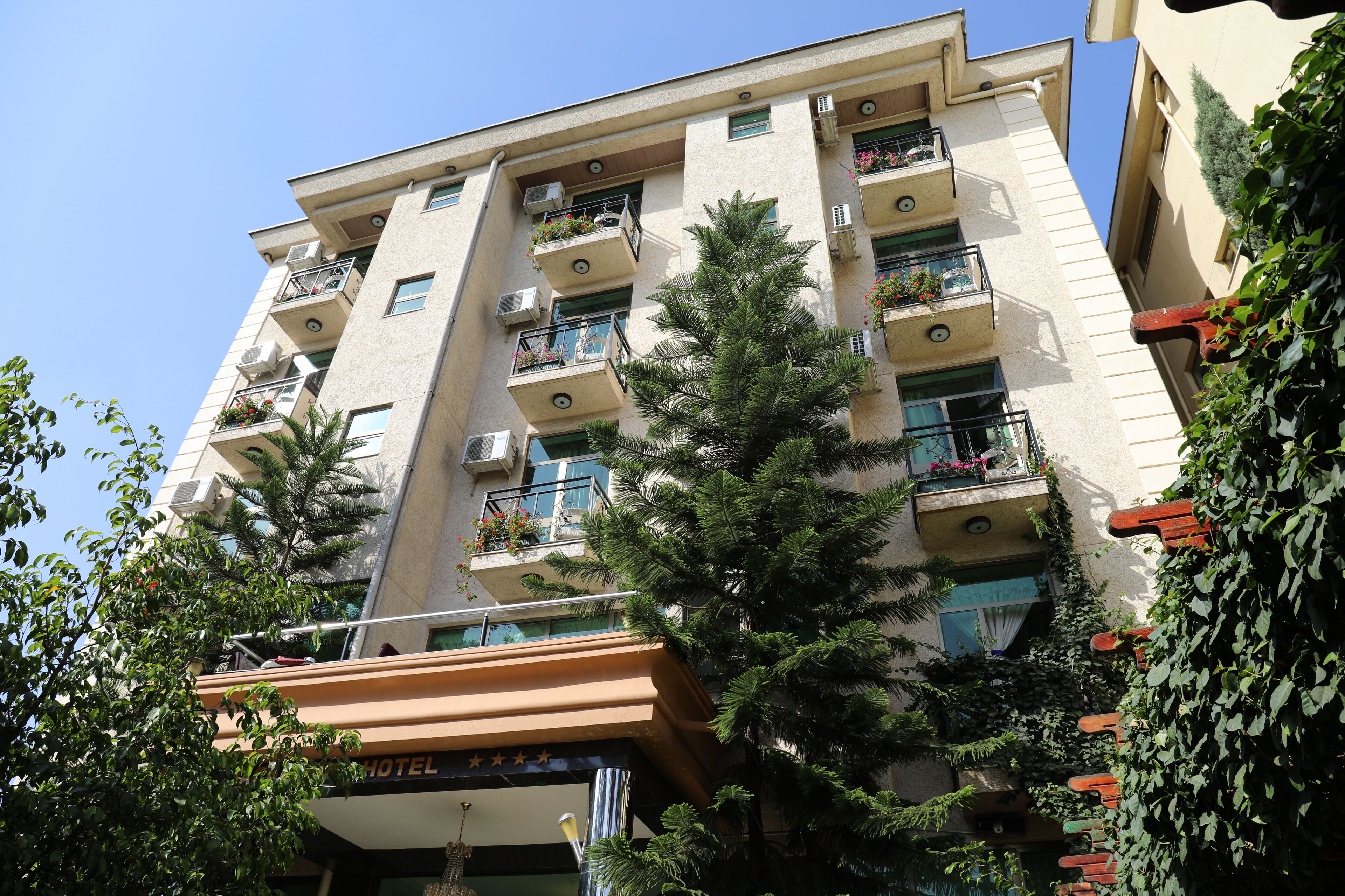 A multi-story hotel with balconies, air conditioning units, and greenery.