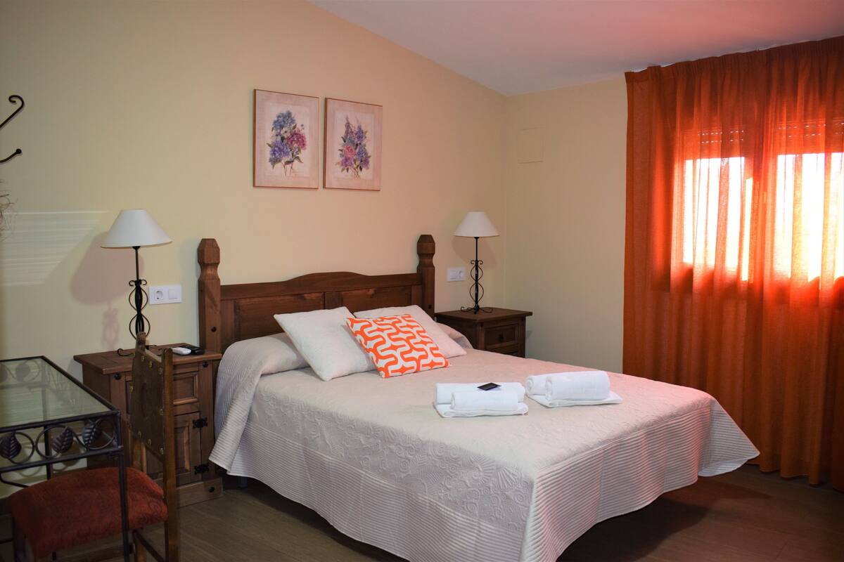 Une chambre d’hôtel bien rangée, avec un grand lit, deux tables de chevet, une chaise et une petite table.