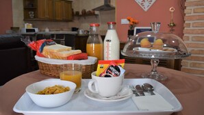 Ett frukostbricka med bröd, flingor, juice och kaffe står på ett bord i ett rum, och i bakgrunden syns ett kök.
