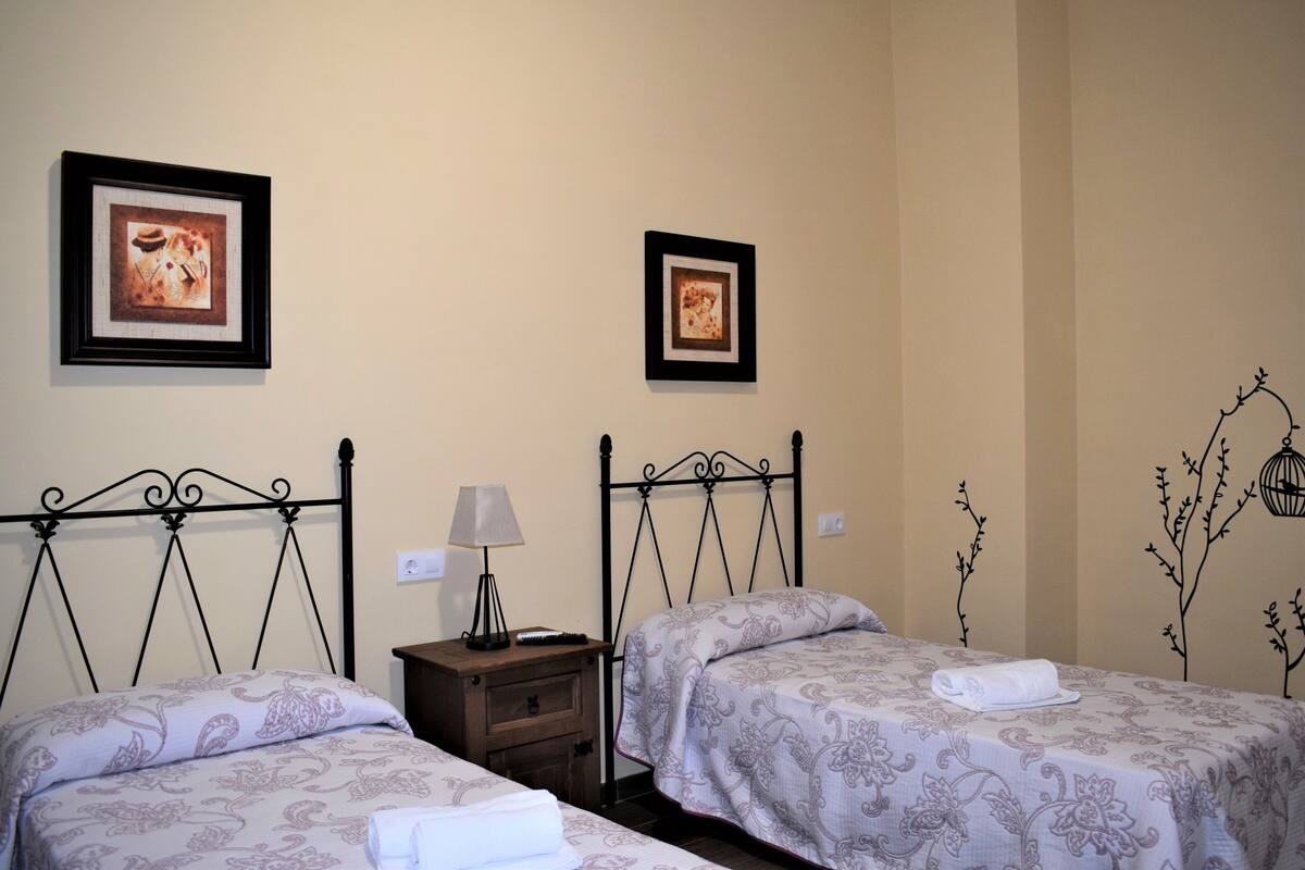Une chambre d’hôtel avec deux lits, chacun recouvert d’une couvre-lit à motifs, une table de chevet avec une lampe et des tableaux encadrés accrochés au mur.