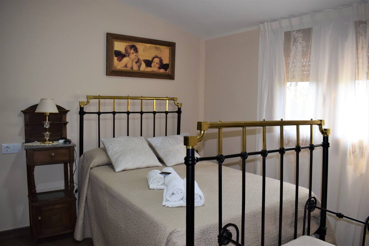 Un lit bien fait, avec une tête de lit, une table de chevet sur laquelle se trouve une lampe, et un tableau accroché au mur.