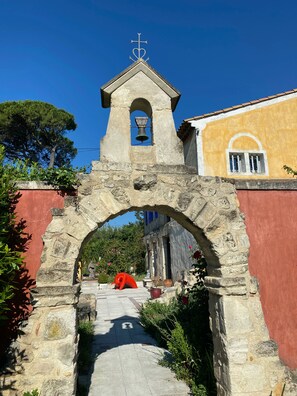 An archway leading to a building with a bell tower, stone walls, and a clear blue sky. - Le Clos de l'isle (Arles)