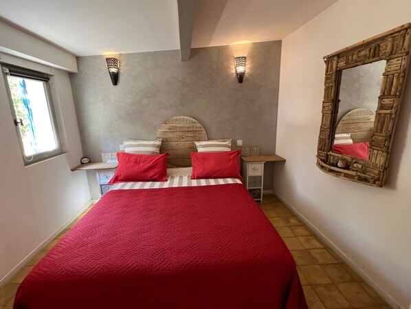 A bedroom with a bed, pillows, a nightstand, a mirror, and a window. - Le Clos de l'isle (Arles)