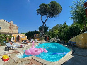 A swimming pool with lounge chairs, a pink inflatable flamingo, and a large tree in the background.