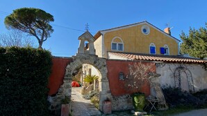 Un edificio amarillo con un arco de piedra en la entrada, una torre de campanas y un árbol grande cerca.