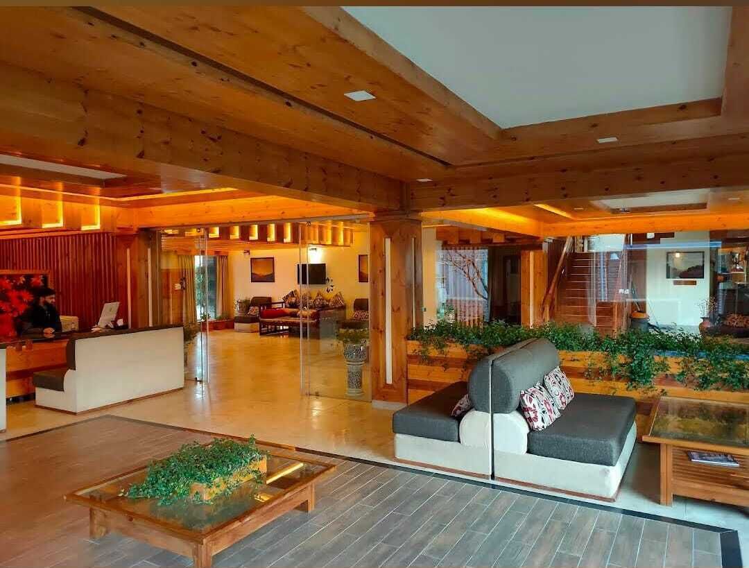 A spacious lobby with wooden beams, a reception desk, a sofa, and a glass coffee table.