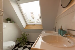 A bathroom with a skylight, two sinks, a toilet, and a potted plant. - Villa Ruth (Reichshof)