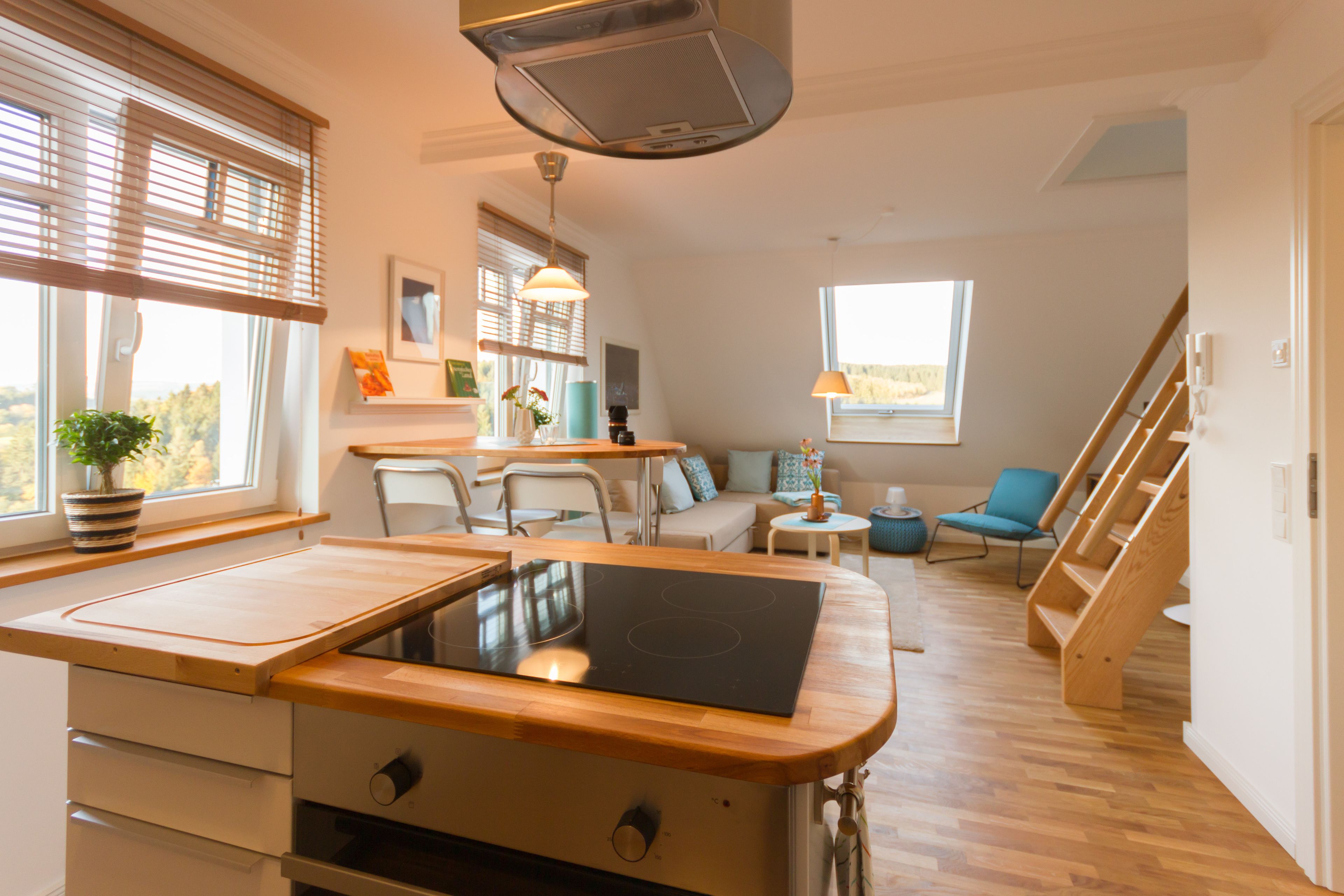 A modern kitchen with a built-in stove, wooden countertops, and a window with blinds.