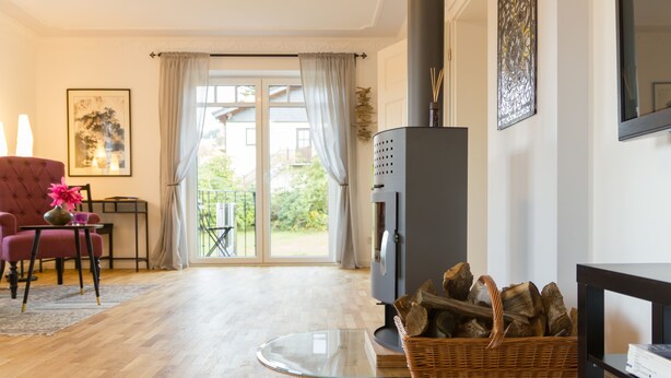 A living room with a fireplace, a red armchair, a glass coffee table, and a wicker basket with logs. - Villa Ruth (Reichshof)