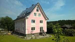 A pink house with solar panels, a front porch, and a well-maintained lawn. - Villa Ruth (Reichshof)