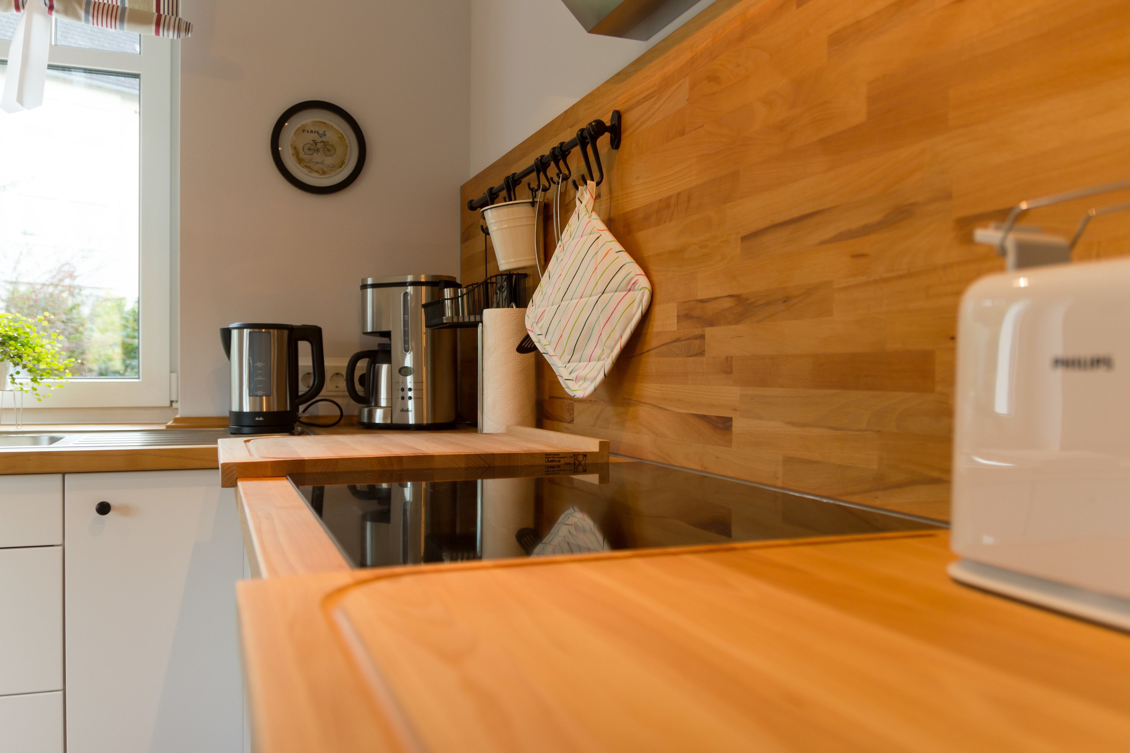 Une cuisine moderne avec des meubles en bois, une machine à café en acier inoxydable, une bouilloire et un grille-pain.