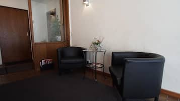 A room with two black leather chairs, a small round table with a vase of flowers, and a wooden door with a glass panel.