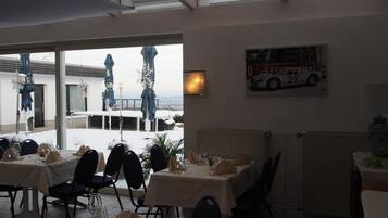 An indoor dining area with tables set for a meal, a large window overlooking a snowy landscape, and a framed picture of a vintage racing car on the wall.
