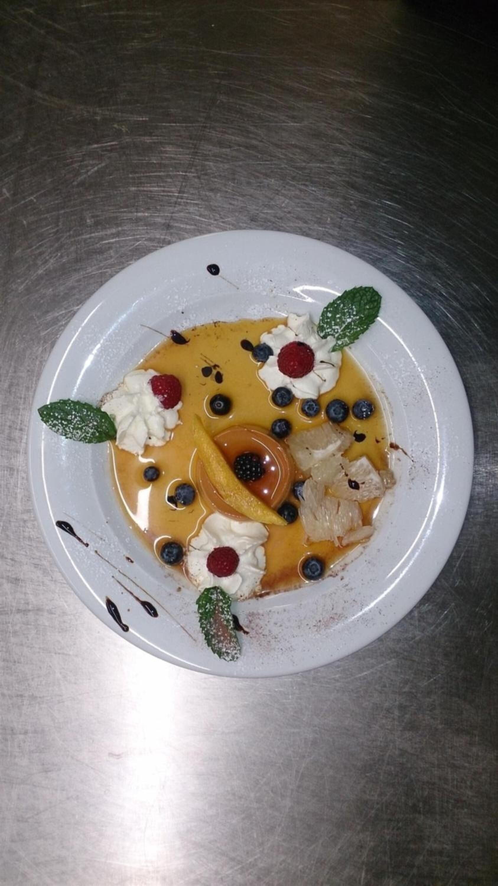 Ein Dessertteller mit Karamellsauce, Schlagsahne, Beeren und einem dekorativen Blatt.