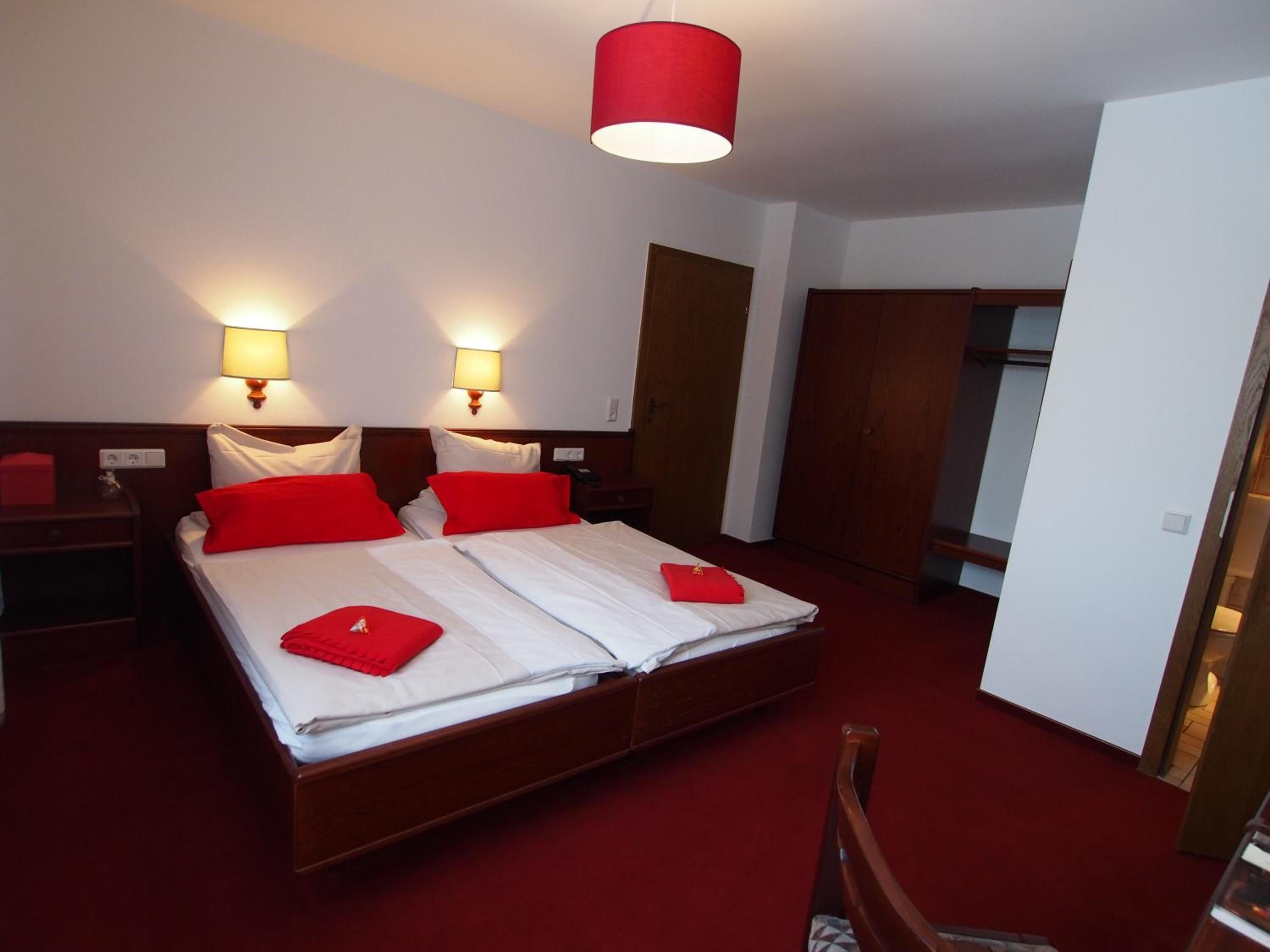 Una habitación de hotel con una cama grande, dos mesitas de noche, un armario y una alfombra roja.