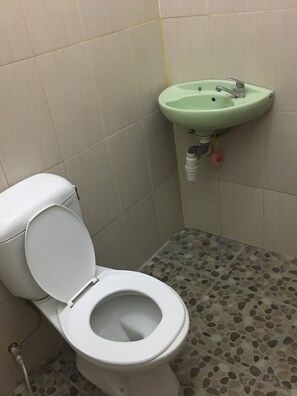 A bathroom with a toilet, a green sink, and a pebble-patterned floor. - Semeton Homestay (Senggigi)
