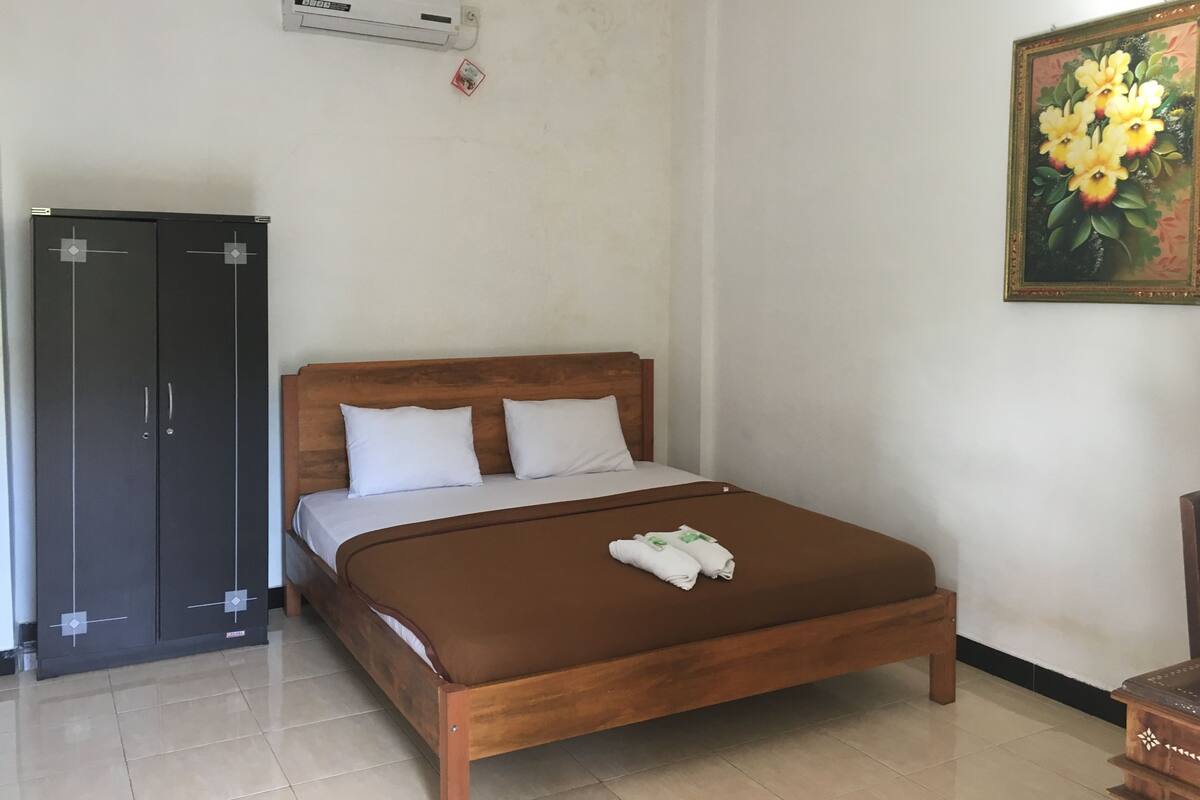 A bedroom with a wooden bed, a wardrobe, an air conditioning unit, and a painting on the wall.
