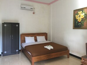 A bedroom with a wooden bed, a wardrobe, an air conditioning unit, and a painting on the wall. - Semeton Homestay (Senggigi)