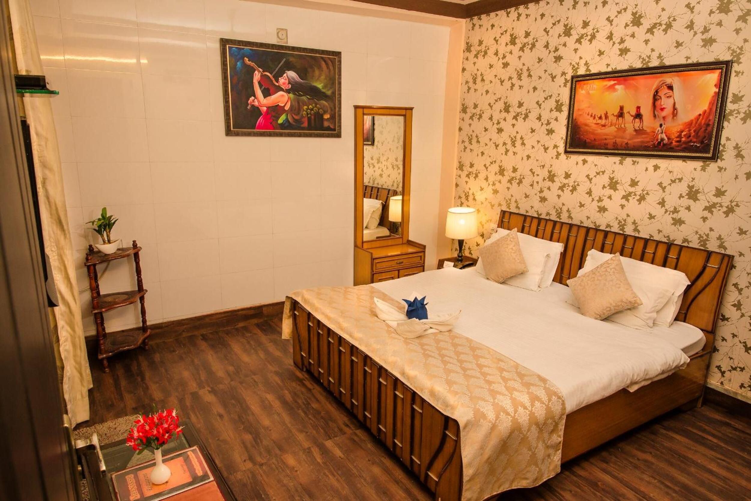 A hotel room with a wooden bed, a nightstand with a lamp, a mirror, and two wall-mounted paintings.