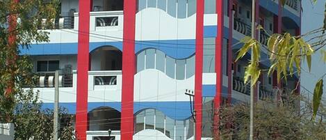 Um hotel de vários andares com fachada distinta em vermelho e azul, varandas e uma placa com a inscrição