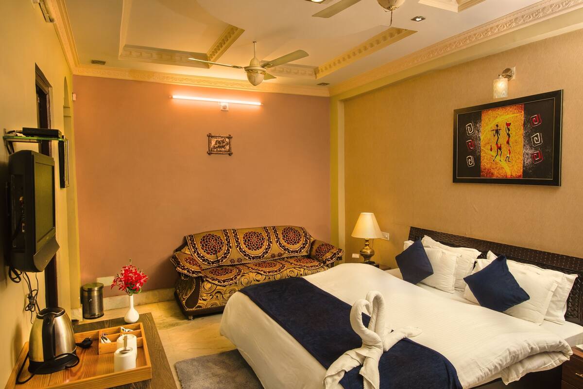 Une chambre d’hôtel avec un lit, un canapé, une télévision, une lampe et un tableau au mur.