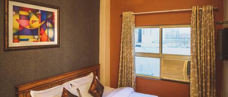 Habitación de hotel con una cama grande, un cuadro abstracto enmarcado, una ventana con cortinas y vistas al exterior.