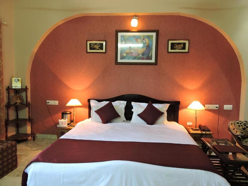 A hotel room with a large bed, two bedside lamps, a painting on the wall, and a small table with a telephone.