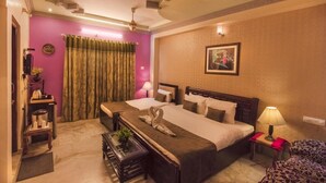 A hotel room with a large bed, a smaller bed, a desk, a chair, a coffee machine, and a window with curtains. - Hotel Meenakshi Udaipur (Udaipur)