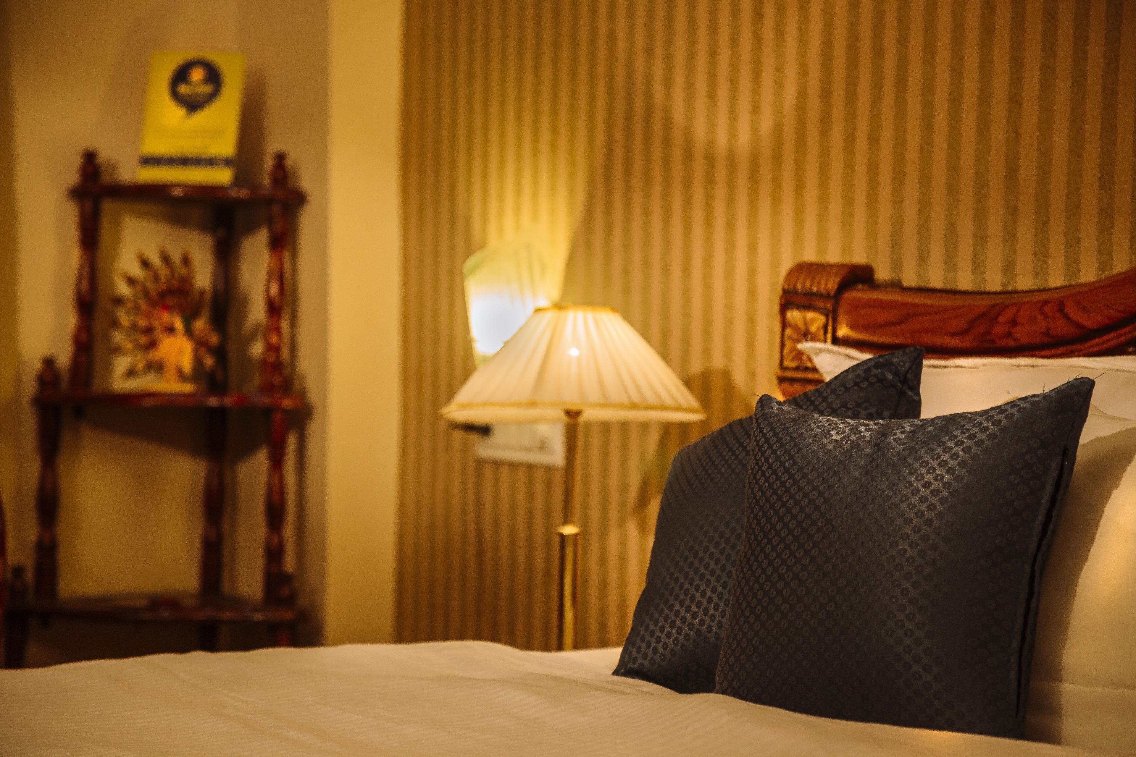A hotel room with a bed, a lamp, a wooden side table with a picture frame, and a striped wall.