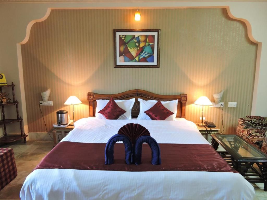 Habitación de hotel con una cama grande, dos lámparas de noche, un cuadro en la pared y un arreglo decorativo de almohadas.