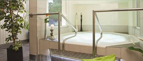 A spa area with a hot tub, metal railings, a potted plant, and a candle.