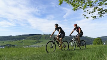 Two cyclists on a grassy hill with a scenic view of rolling hills and a clear sky.