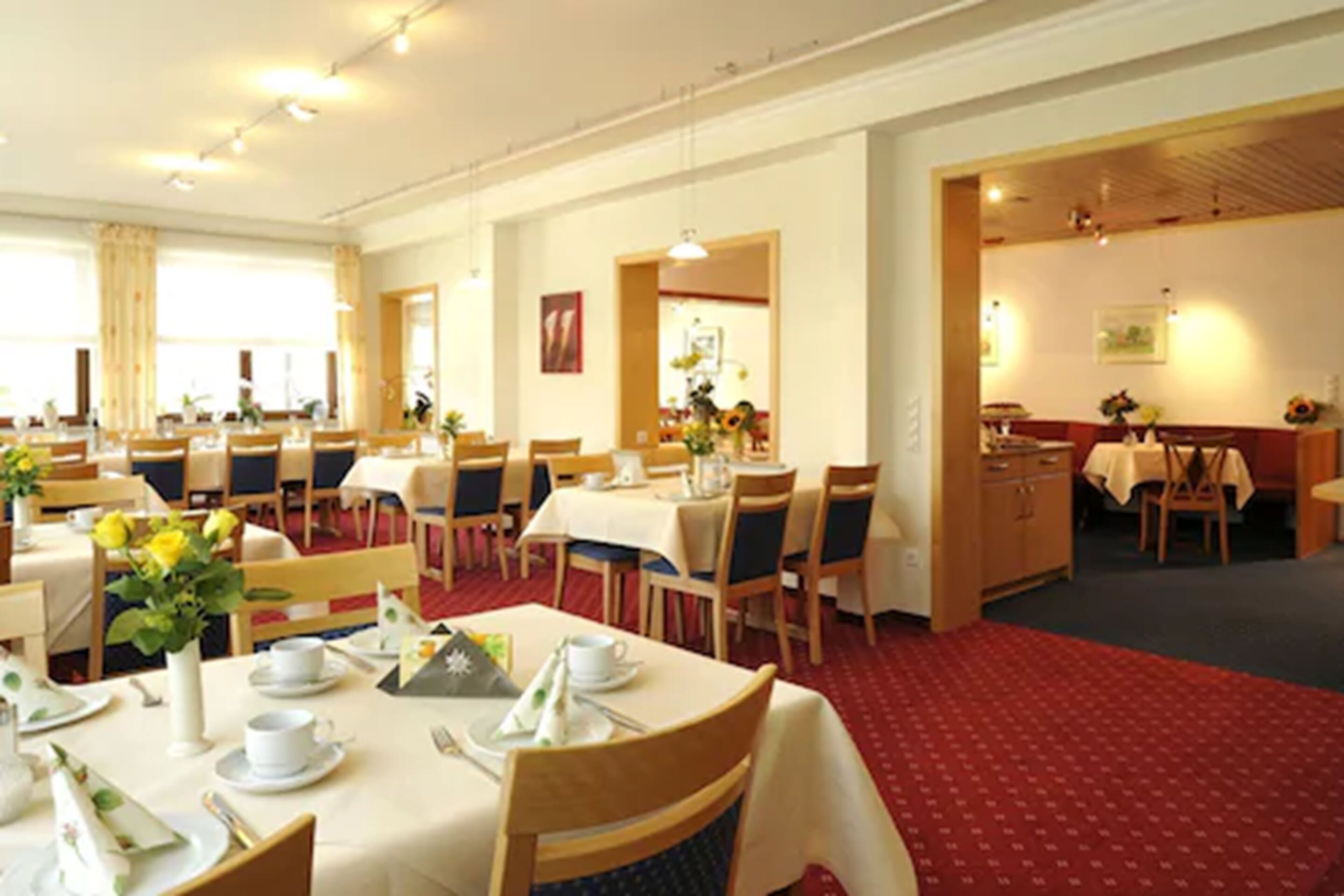 Ein Hotel-Speisesaal mit mehreren für das Frühstück gedeckten Tischen, mit weißen Tischdecken, Stühlen und ordentlich drapierten Frühstücksartikeln.