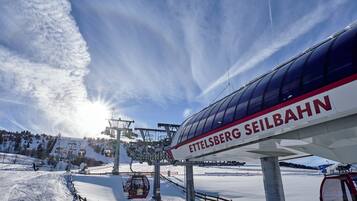 A ski lift with the name "ETTELSBERG SEILBAHN" and a snowy landscape with a clear sky.