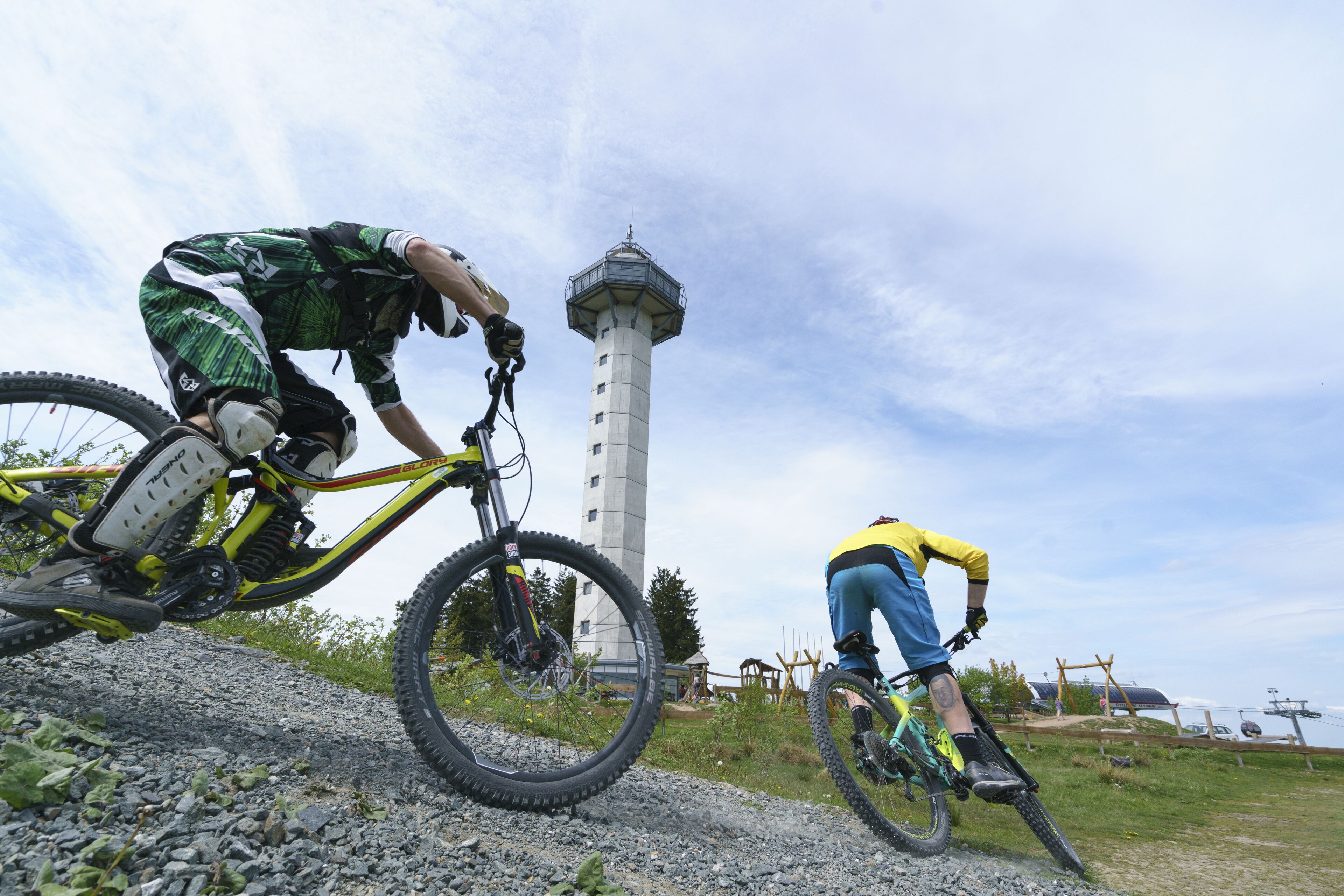 Two mountain bikers on a gravel path with a lighthouse in the background.