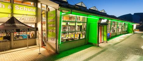 A brightly lit storefront with a green neon sign and a visible shop window.