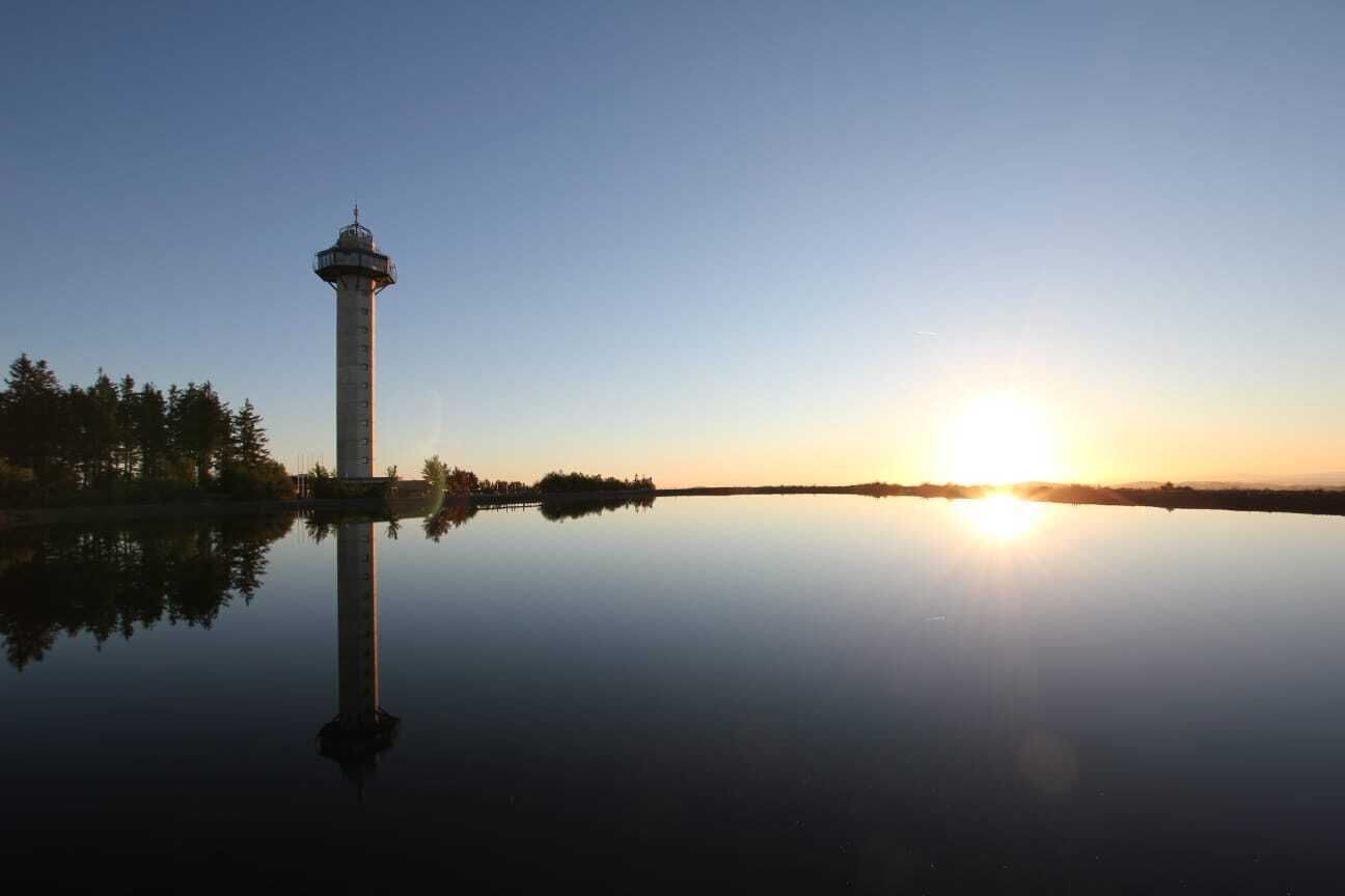 A lighthouse by a calm lake at sunrise.