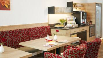 Comedor con mesa de madera, sillas tapizadas en rojo y zona de cocina con refrigerador y microondas.